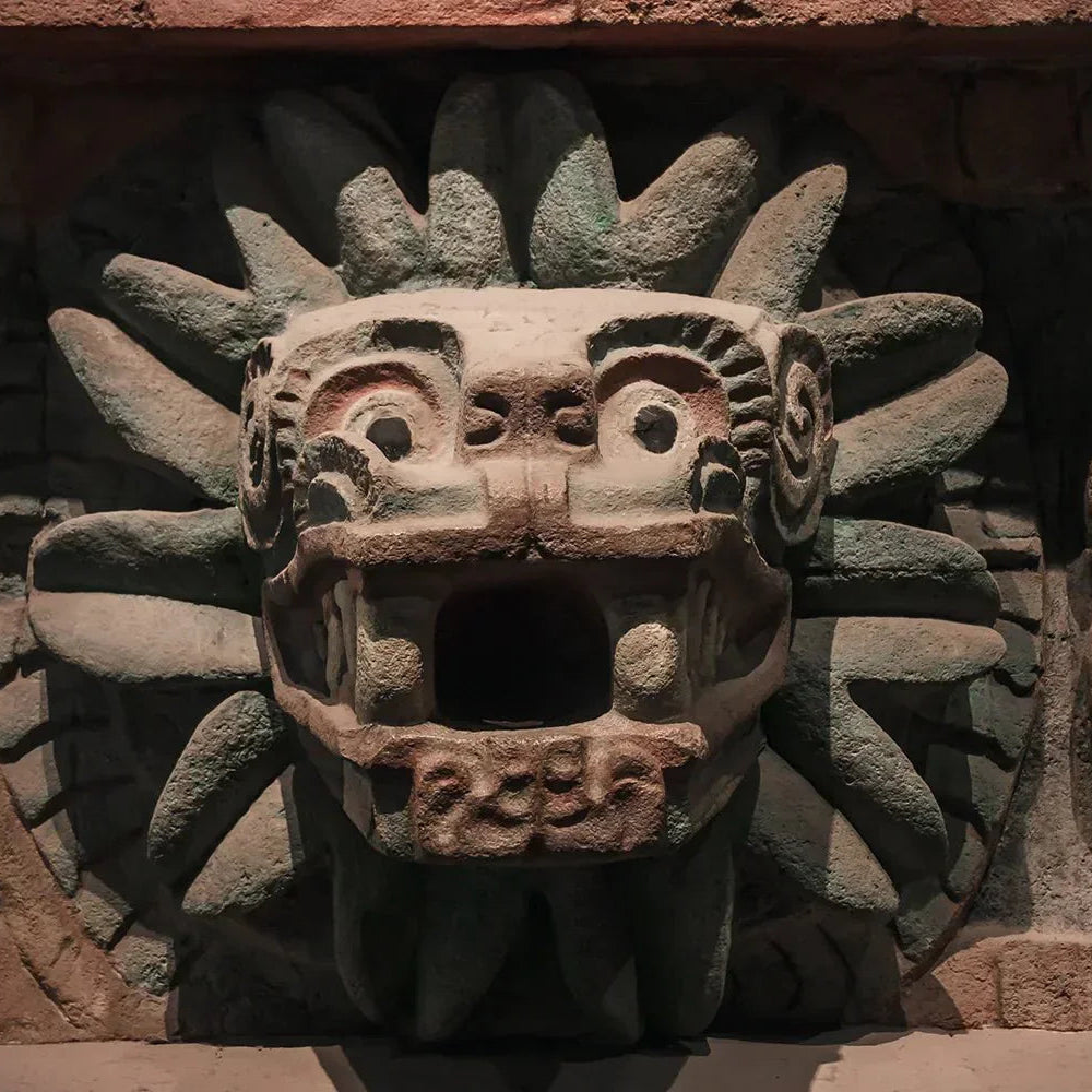 An ancient Mayan-style stone sculpture of a sun face carved into a reddish-brown stone wall.